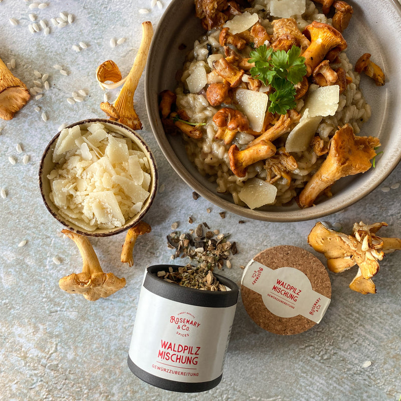 Eine Schüssel Pilzrisotto mit frischen Pfifferlingen, daneben eine Schale Parmesan und eine Dose mit Waldpilzmischung.