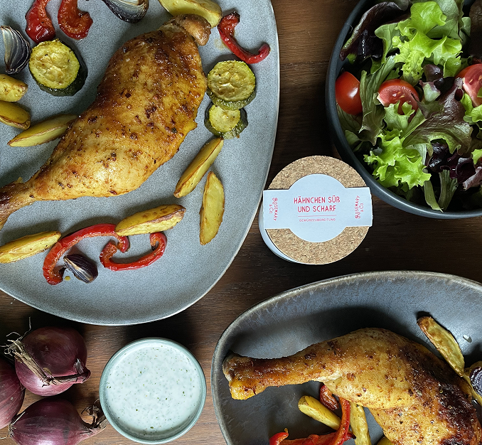 Tisch mit Hähnchenschenkeln, Gemüse, Salat, Gewürzdose und einer kleinen Schale Dip.