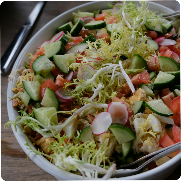 Ein Teller mit frischem Salat aus Gurken, Tomaten, Radieschen und Salatblättern, auf einem Holztisch serviert.