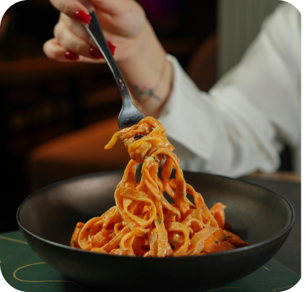 Eine Hand mit rotem Nagellack hält eine Gabel mit Spaghetti in einer schwarzen Schüssel.