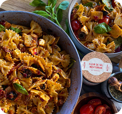 Zwei Schüsseln mit Pasta-Salat, dekoriert mit Basilikumblättern, neben einer Pappdose mit der Aufschrift "Fleur de Sel Mediterran".