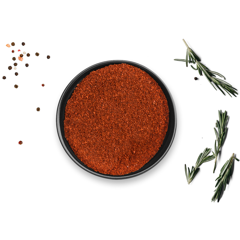Auf weißem Untergrund steht eine schwarze Schale mit Bio Paprika Geräuchert von Rosemary & Co. Gewürze, umgeben von verstreuten Pfefferkörnern und Rosmarinzweigen.