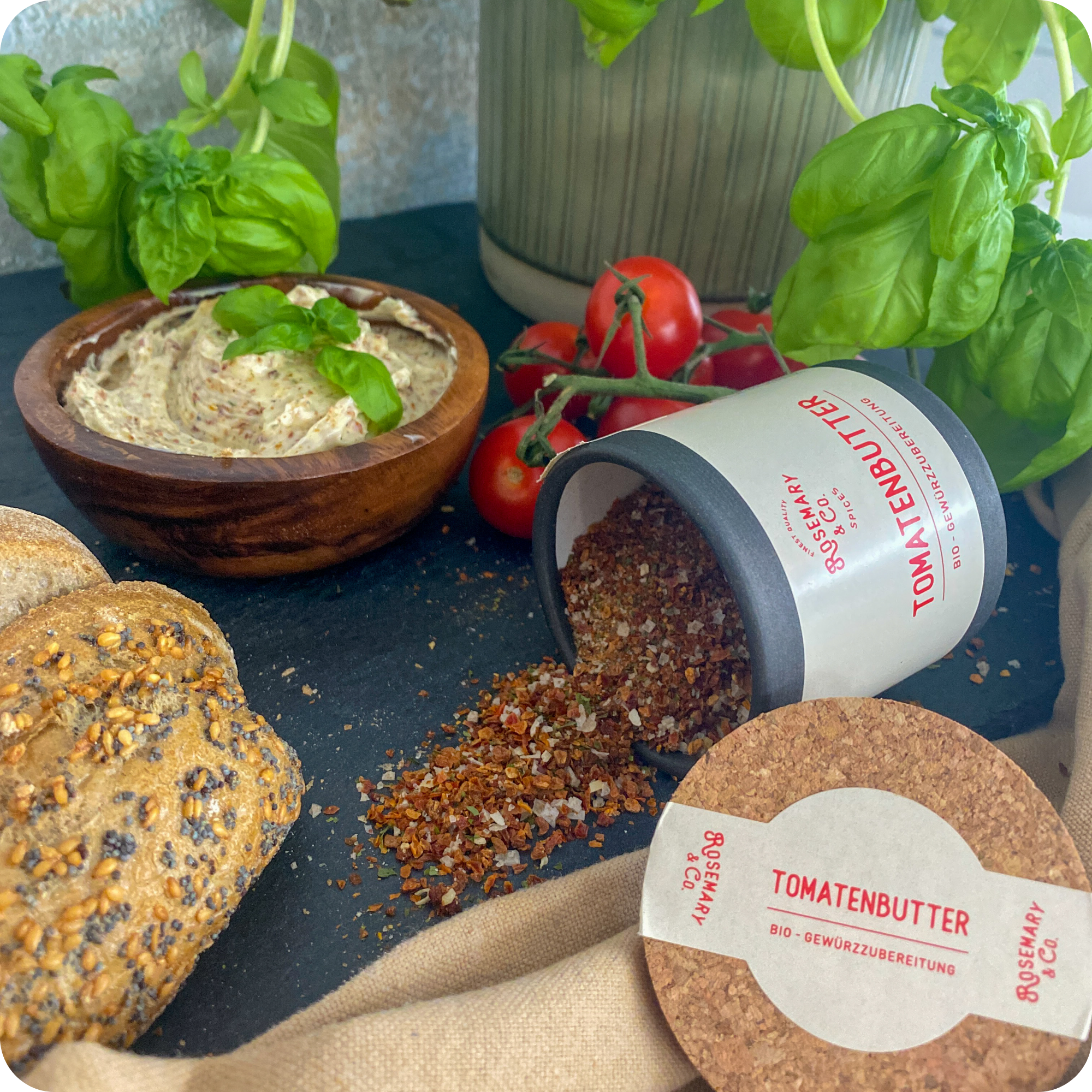 Dose Tomatenbutter Gewürzmischung Bio von Rosemary & Co, verschüttet neben Brot, Dip, Tomaten und Basilikum