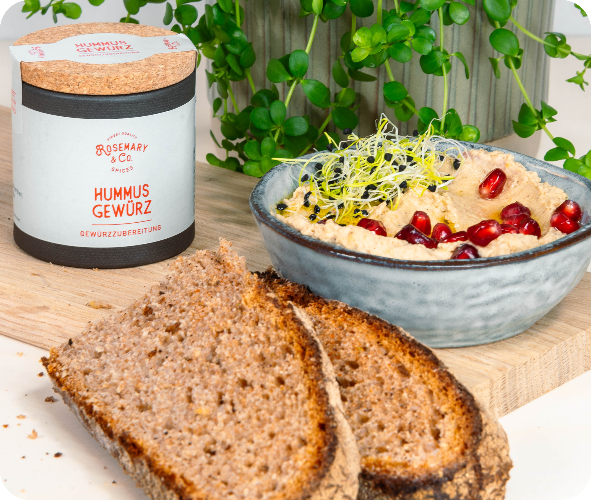 Schale Hummus mit Sprossen, Granatapfelkernen, Brot und Dose Rosemary & Co. Hummus Gewürze auf Tisch