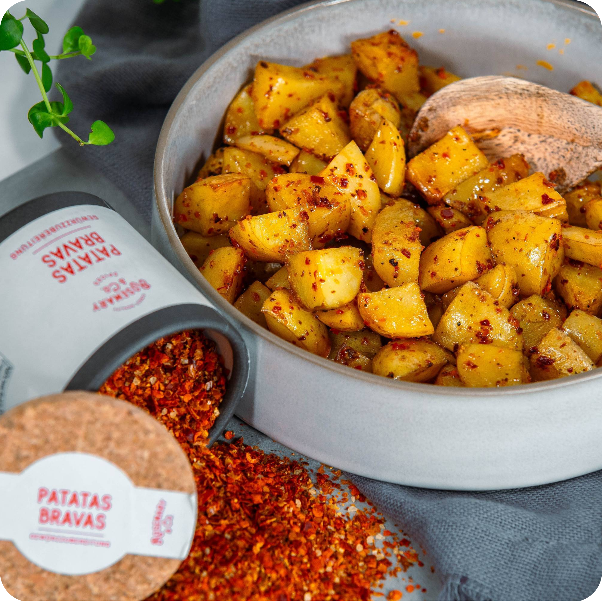 Geröstete Kartoffelwürfel mit rotem Gewürz neben umgekippter Dose Rosemary & Co. Patatas Bravas