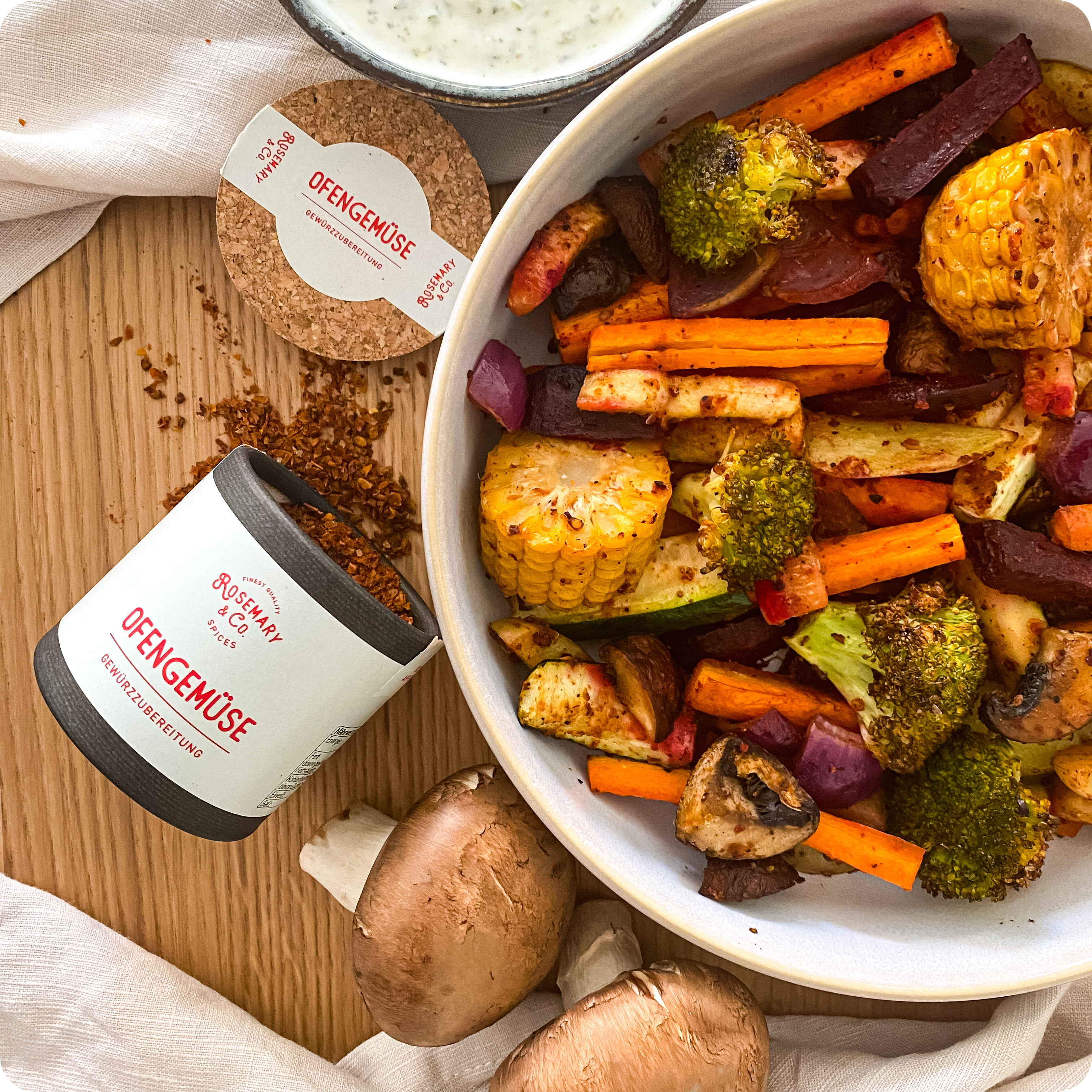 Schale mit Ofengemüse, Dose Rosemary & Co. Gewürze Ofengemüse, zwei Champignons auf Holz