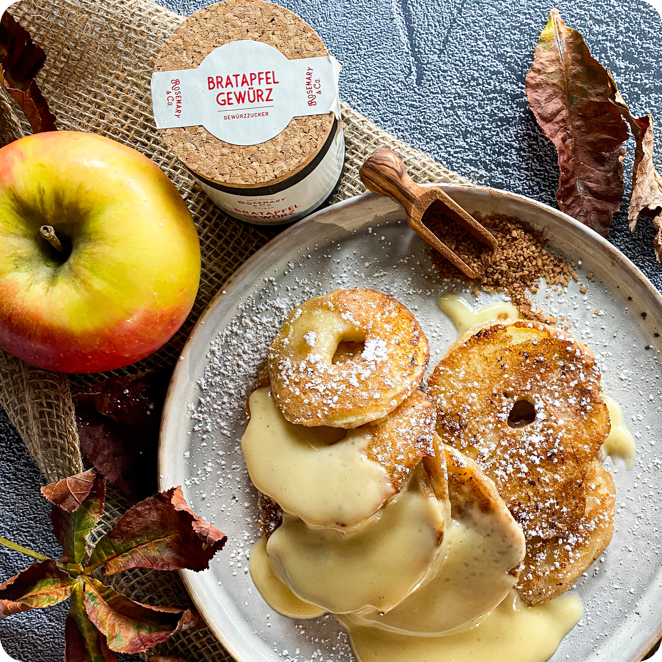 Apfelkrapfen mit Cremesauce und Bratapfel Gewürze von Rosemary & Co., serviert mit Apfelscheiben und Herbstblättern