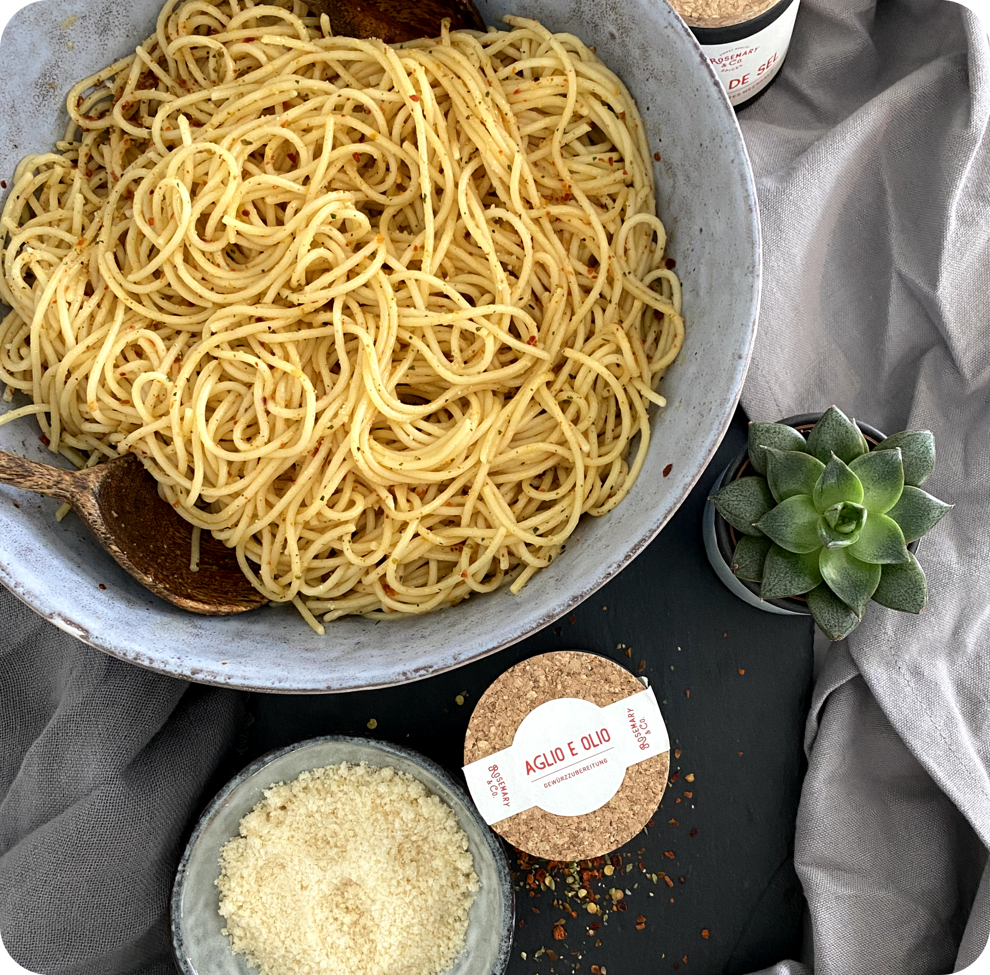 Schüssel mit Spaghetti, Holzzange, geriebenem Käse, Dose Rosmarin & Co. Gewürze Aglio e Olio, Sukkulente