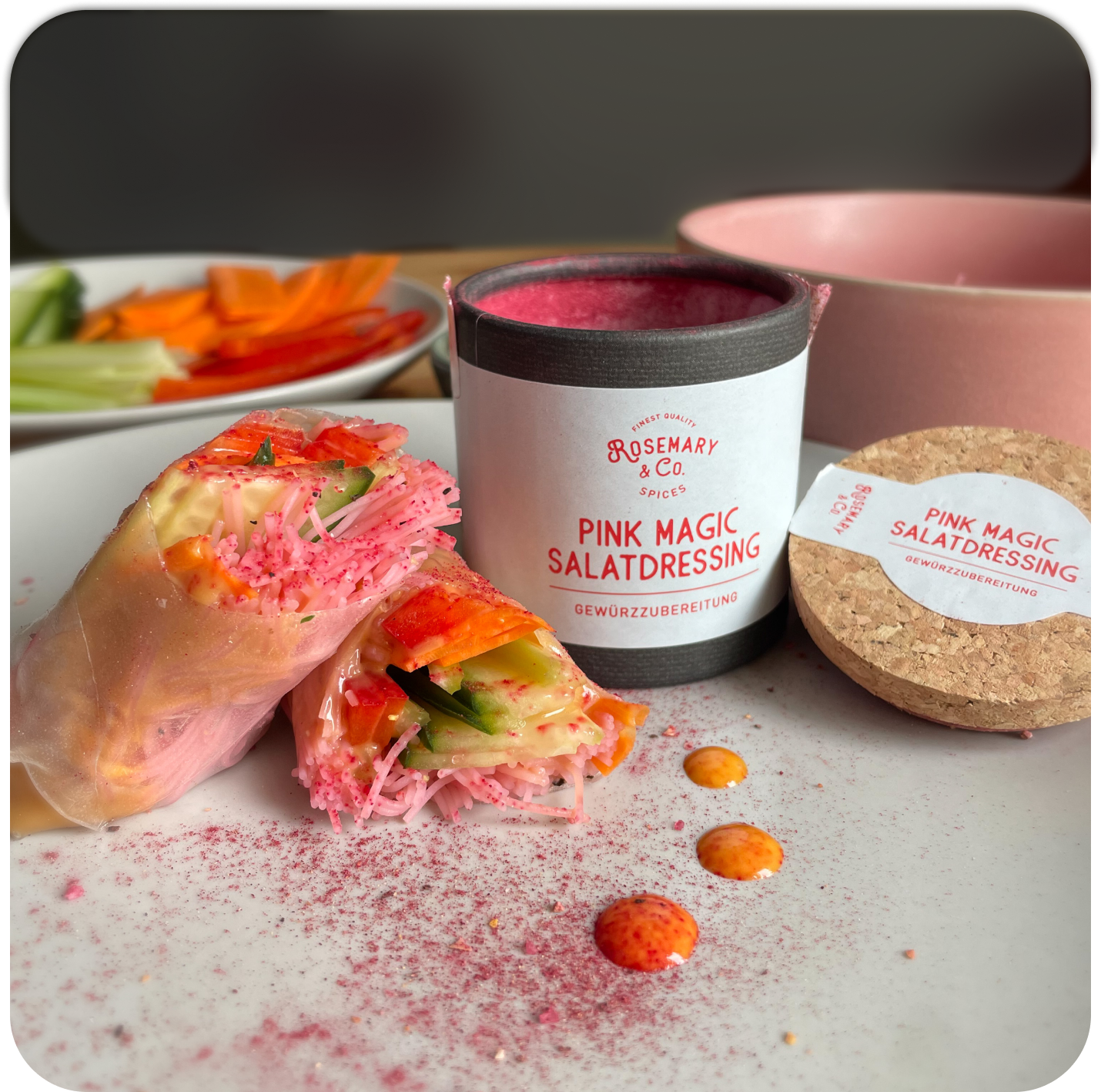 Zwei Gemüse-Frühlingsrollen neben Dose Rosemary & Co. Gewürze Pink Magic Salatdressing, Gemüse im Hintergrund